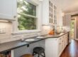 Narrow white kitchen with dark countertops and a built-in window breakfast bar