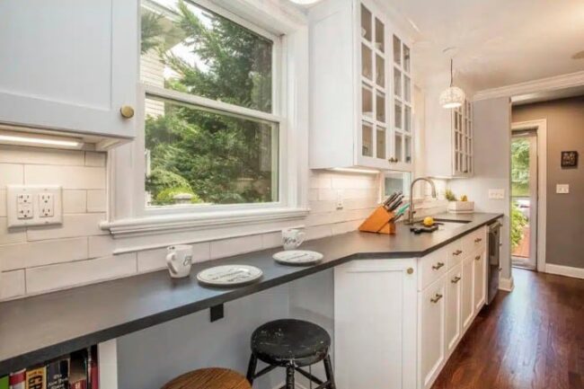 Narrow white kitchen with dark countertops and a built-in window breakfast bar