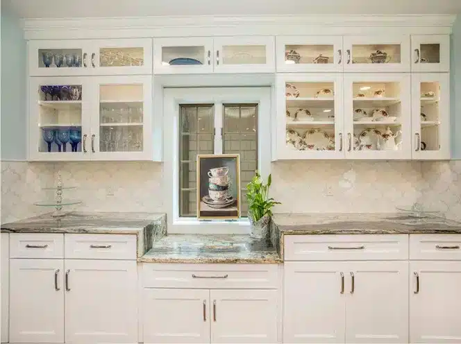 White shaker-style kitchen cabinets with integrated glass front display doors over a window