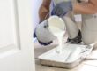 Painter pouring white paint into a roller tray during a home renovation