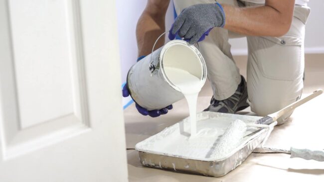 Painter pouring white paint into a roller tray during a home renovation